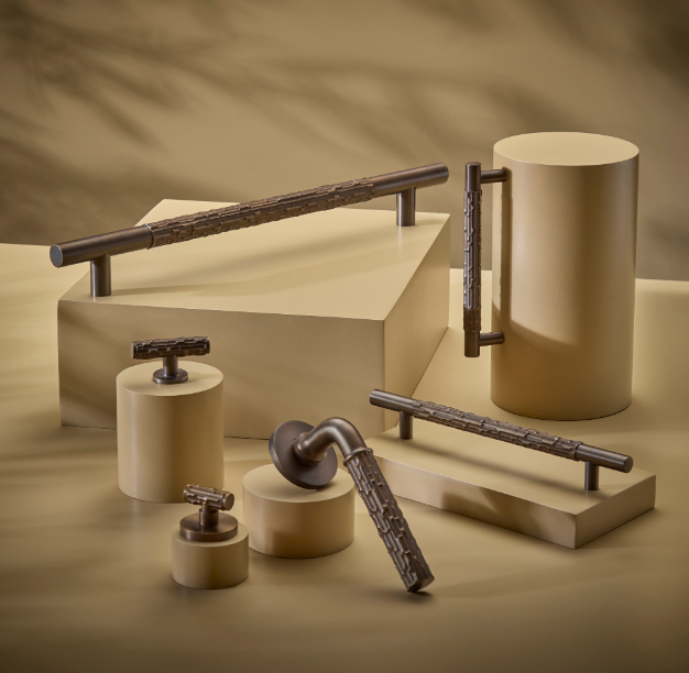 Featured image of latest British-made hardware collection, displaying coordinated dark bronze cabinet handles, pull bars, and a textured lever door handle arranged on neutral display plinths.