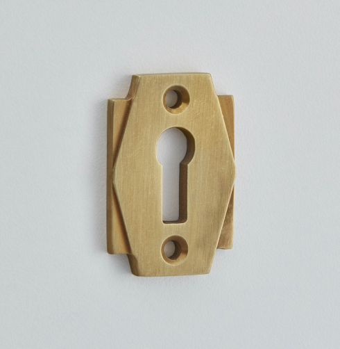 Art Deco style furniture hardware escutcheon in polished metal with geometric stepped design.