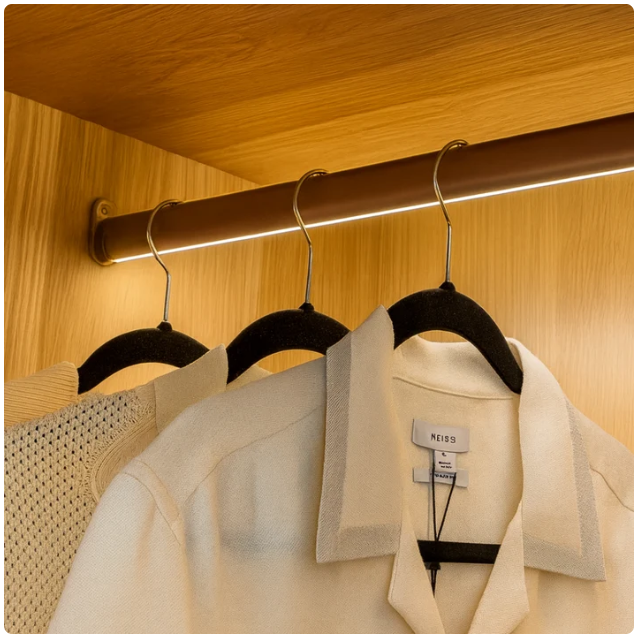 LED Wardrobe Rail illuminating clothing inside a luxury fitted wardrobe.
